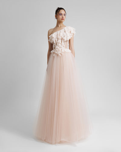 A one-shoulder cut corset evening dress in blush color, with ruffled details on the bodice part, see through fabric on the waist, and a tulle skirt.