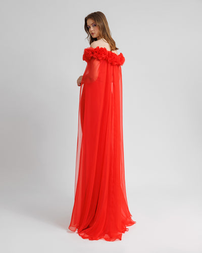 The back of a draped flower embellishment off-the-shoulders, straight-cut red evening dress, with a flowy chiffon cape-like sleeves.