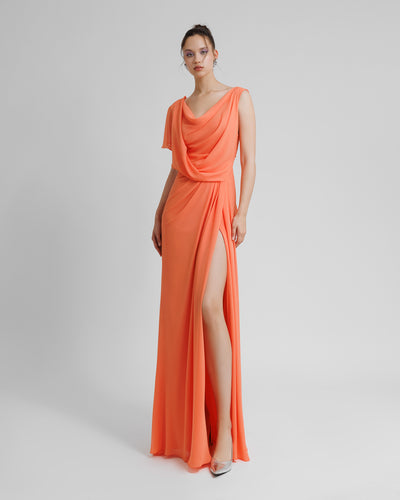 A draped long peach evening dress with asymmetrical sleeves, and a high slit on the side.