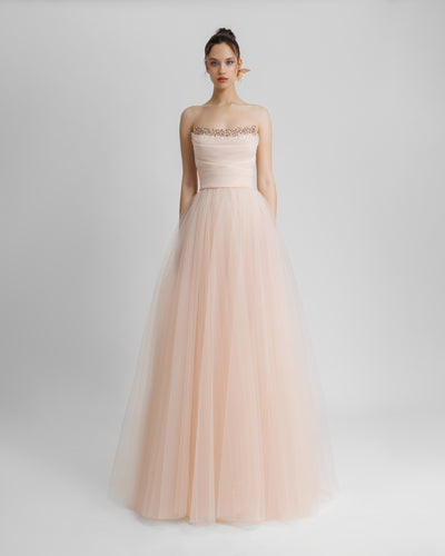 A strapless, flared long blush evening dress with beading and draping details on the bust line.