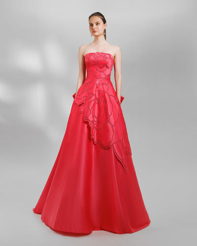 A strapless red evening dress with laser-cut details, a wide flared cut, and draping at the back.