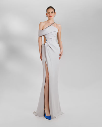 A long crepe asymmetrical neckline grey dress, featuring beadings on the neckline and an open side waist with beads and draping. The dress features a high side slit as well.