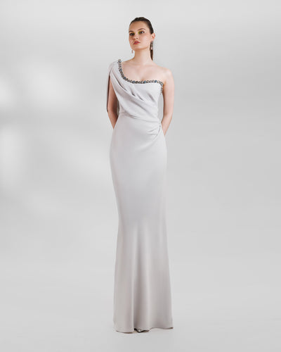 A one-shoulder beaded neckline long grey evening dress featuring draping details on the bust and waist highlighting the body curves.