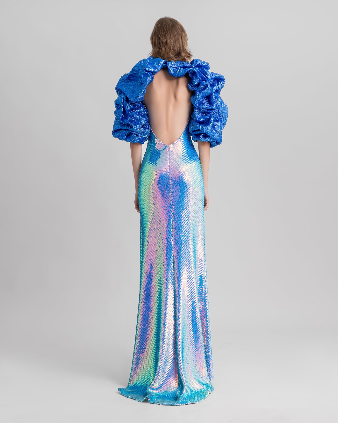 A halter-neck slim-cut evening dress fully sequined in blue with a low open back, paired with a draped bolero.