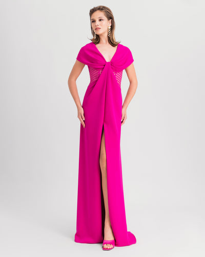 A v-neckline fuchsia evening dress with draped bow-like shoulders, crochet lace sides, and a slit at the front.