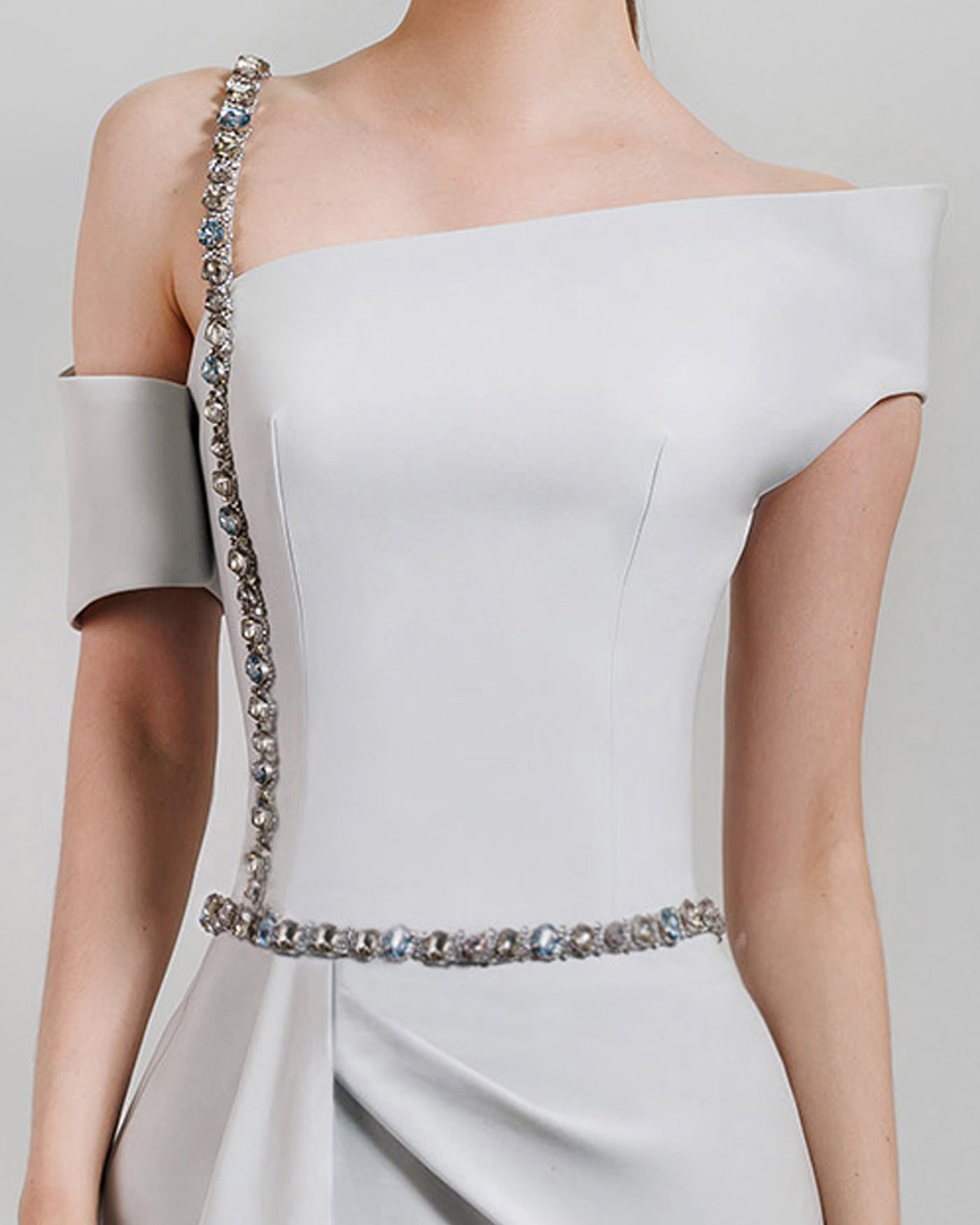 A close-up of an asymmetrical neckline grey dress with a beaded strap paired with a draped skirt featuring a slit on the side and a detachable belt.