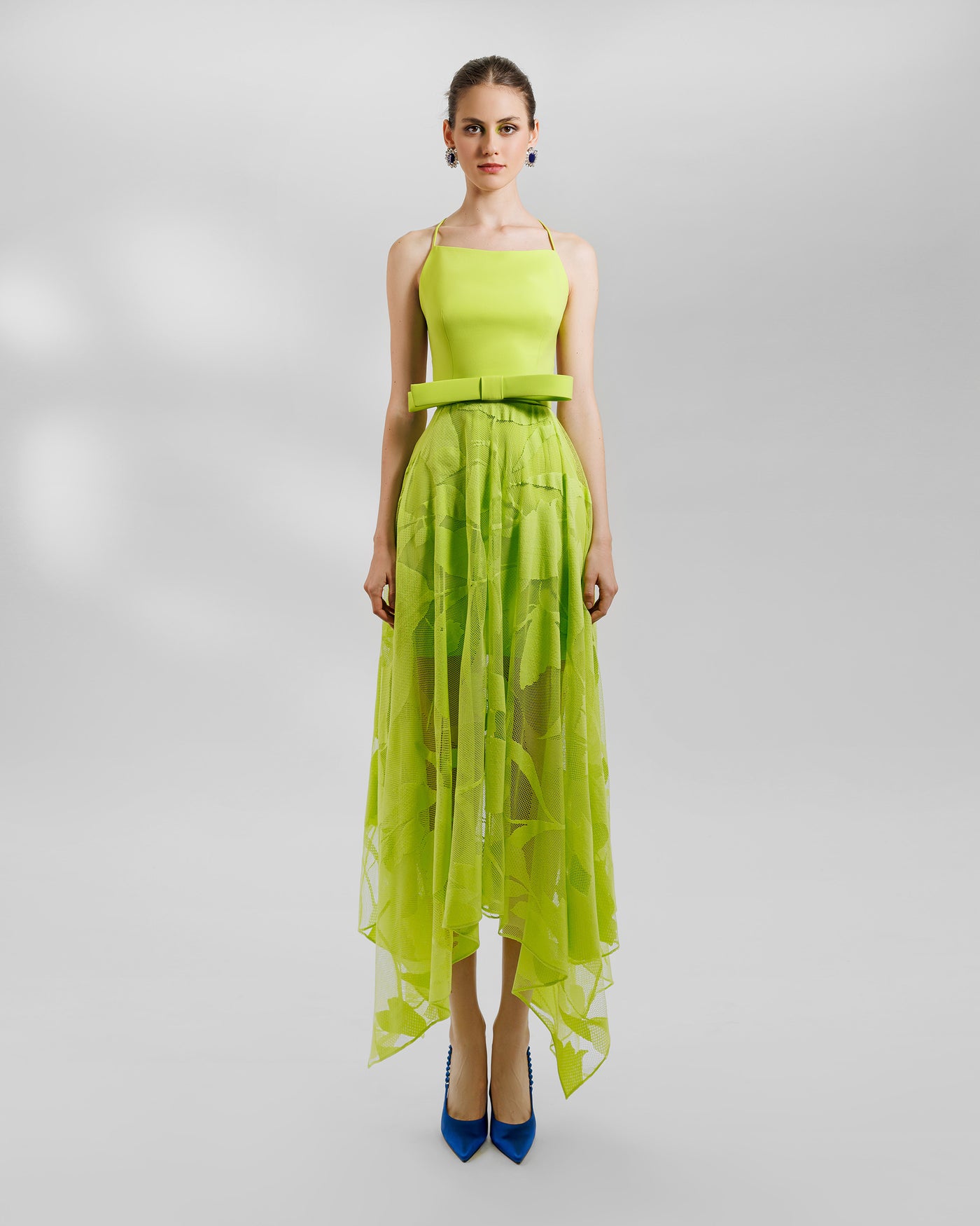 An evening wear set featuring a patterned lace midi skirt with asymmetrical hemline, and a crepe top with a sharp bow design, all in lime color.