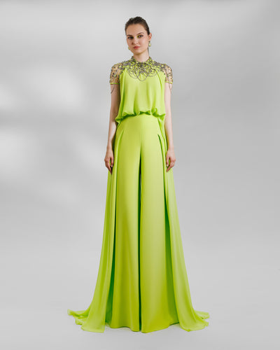 An evening wear set in lime color featuring an embellished crepe georgette shoulders cape-like top that has a high beaded neckline, it is paired with a crepe high-waist wide pants that has some pleats on both sides.