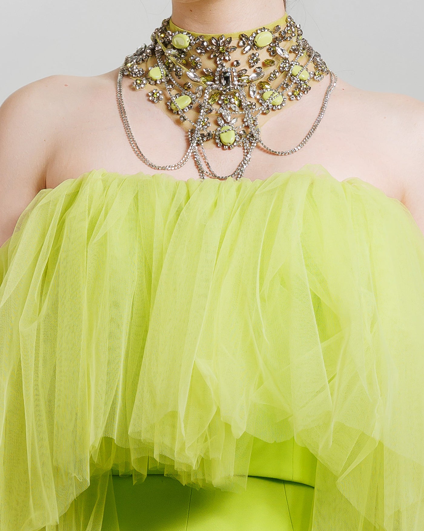 A close-up of an evening look in lime color featuring an off-the-shoulders tulle top. The look is completed with a matching beaded collar necklace.