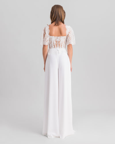 The back of a white evening wear set featuring an open back lace top with flared sleeves paired with flared pants.