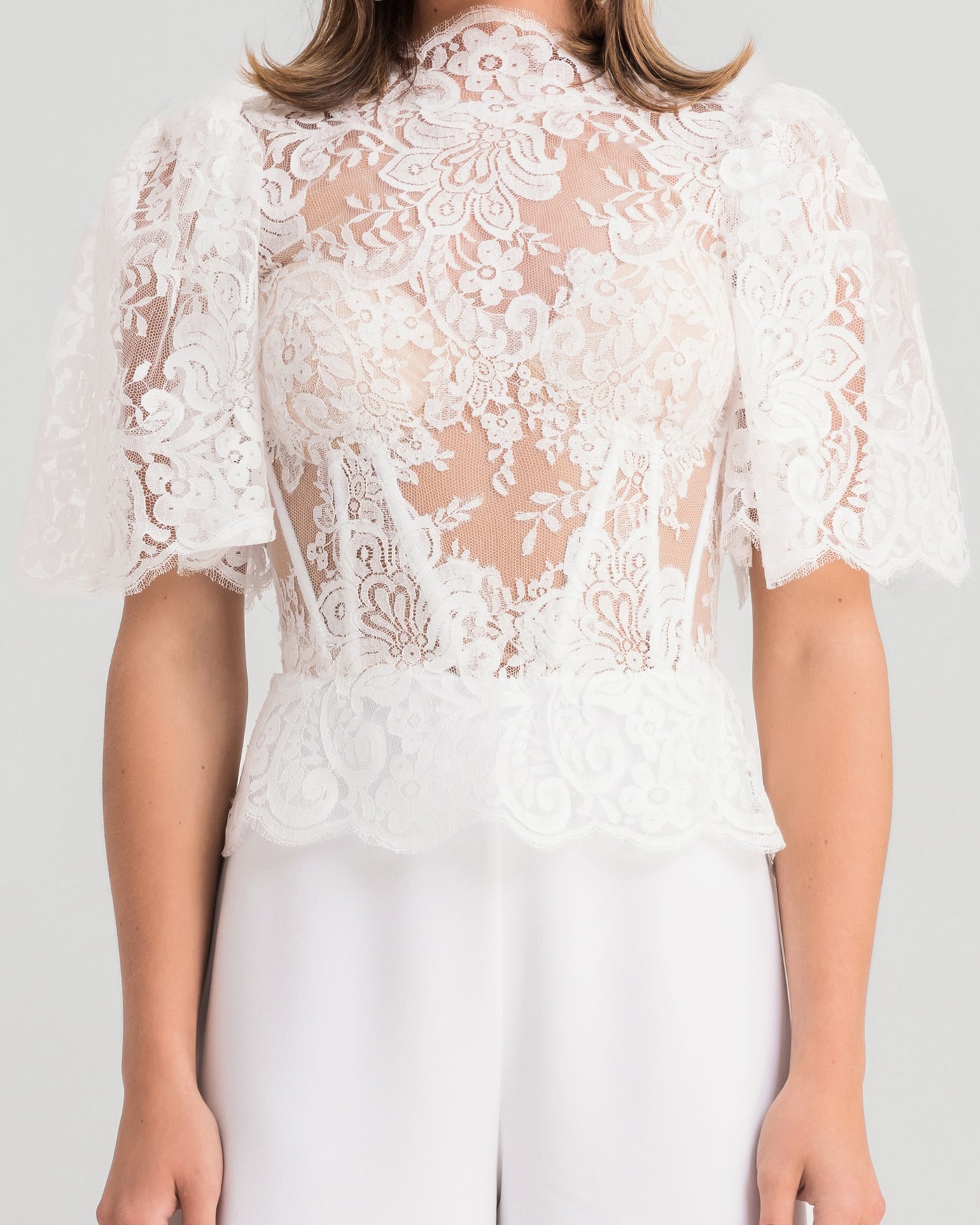 A close-up of a white evening wear set featuring a high-collar lace top with flared sleeves paired with flared pants.