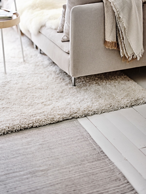 A living room with a white wooden floor has a TIPHEDE rug, a VOLLERSLEV rug, and a SÖDERHAMN 1-seat section on it.