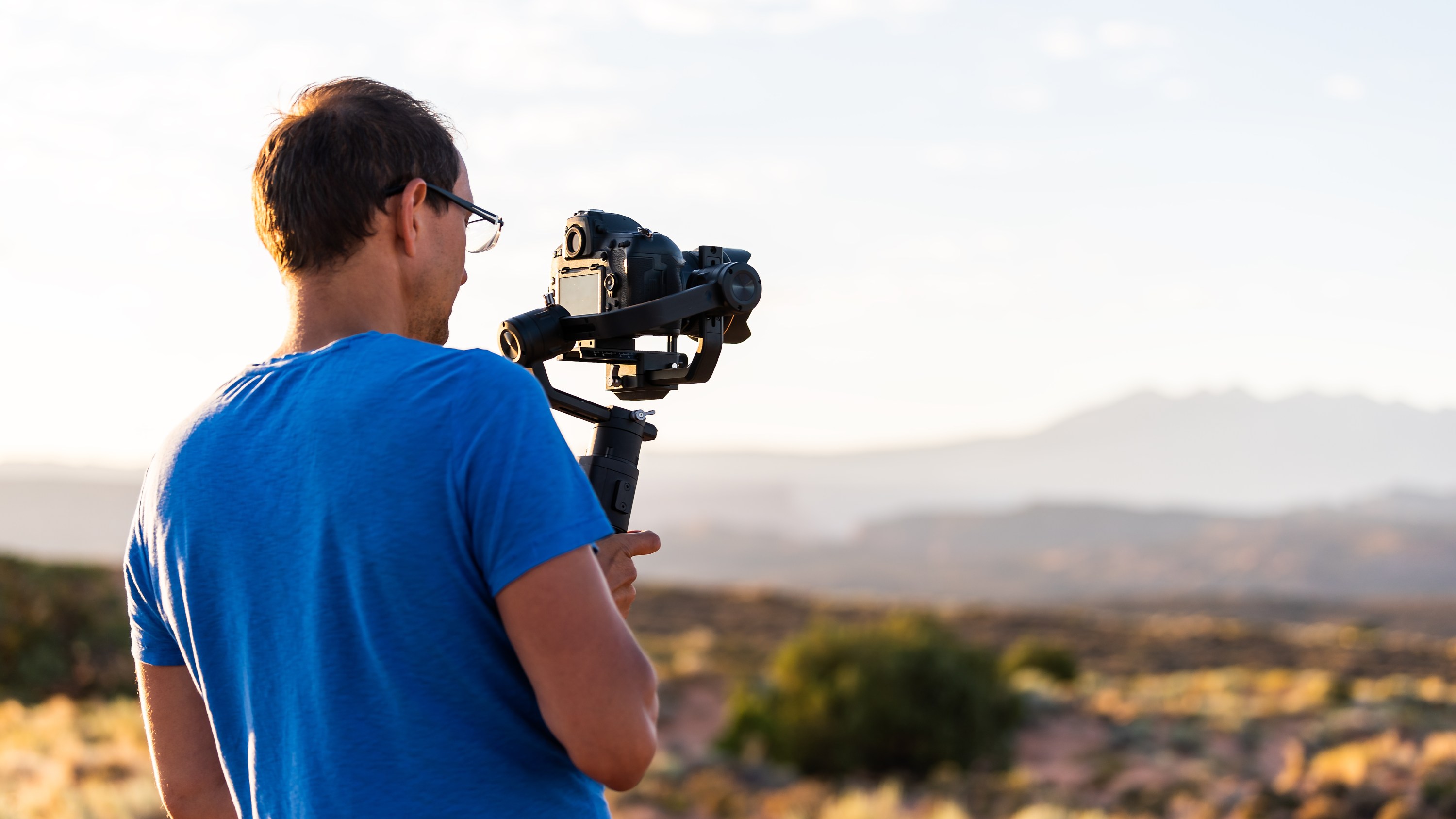 Man holding gimbal camera stabilizer filming valley view of sunrise with sunlight rays in Arches National Park, Utah, USA morning at Fiery Furnace Viewpoint