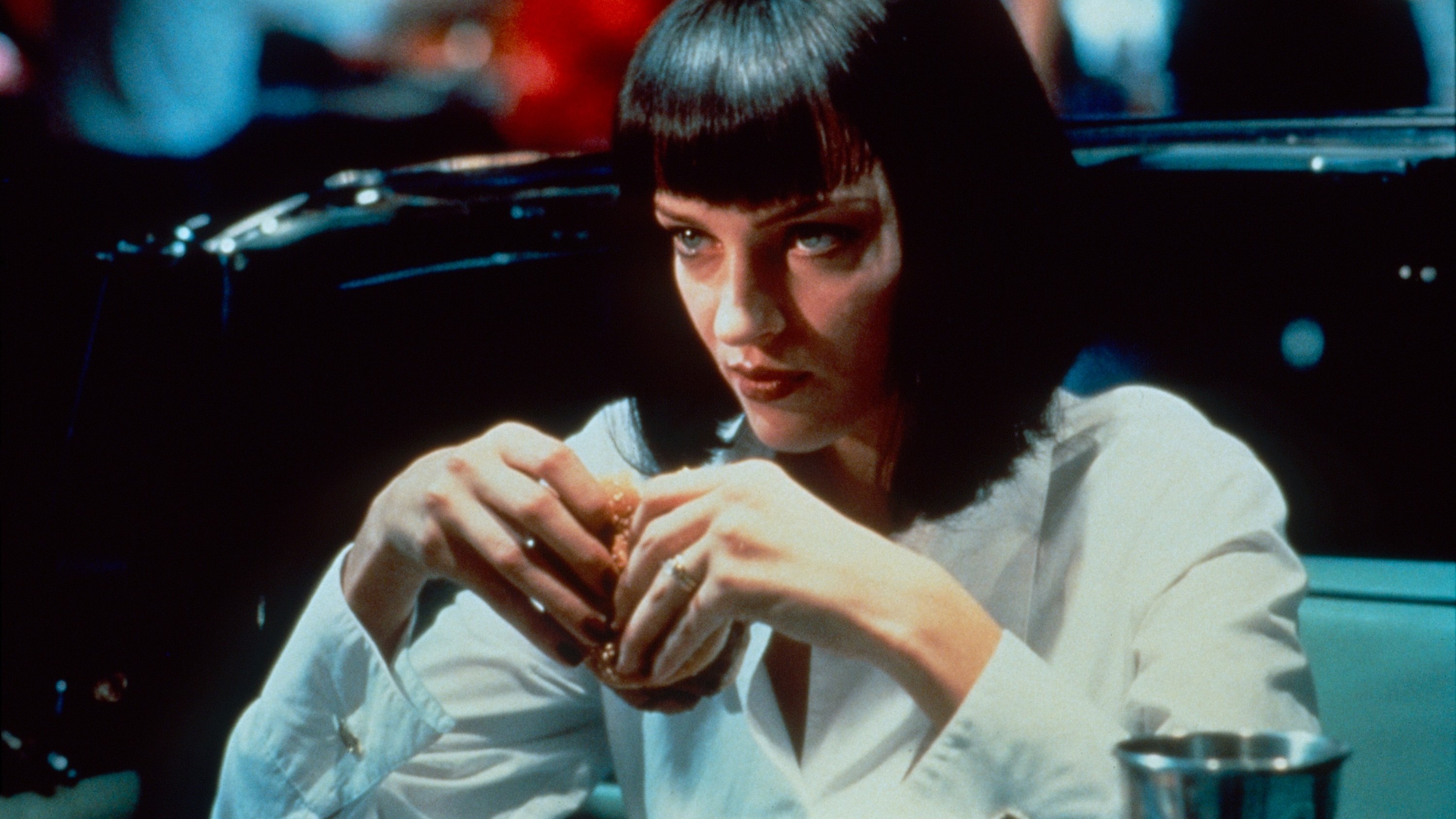 A woman with short black hair wearing a collared shirt and holding a burger; Uma Thurman in 'Pulp Fiction'