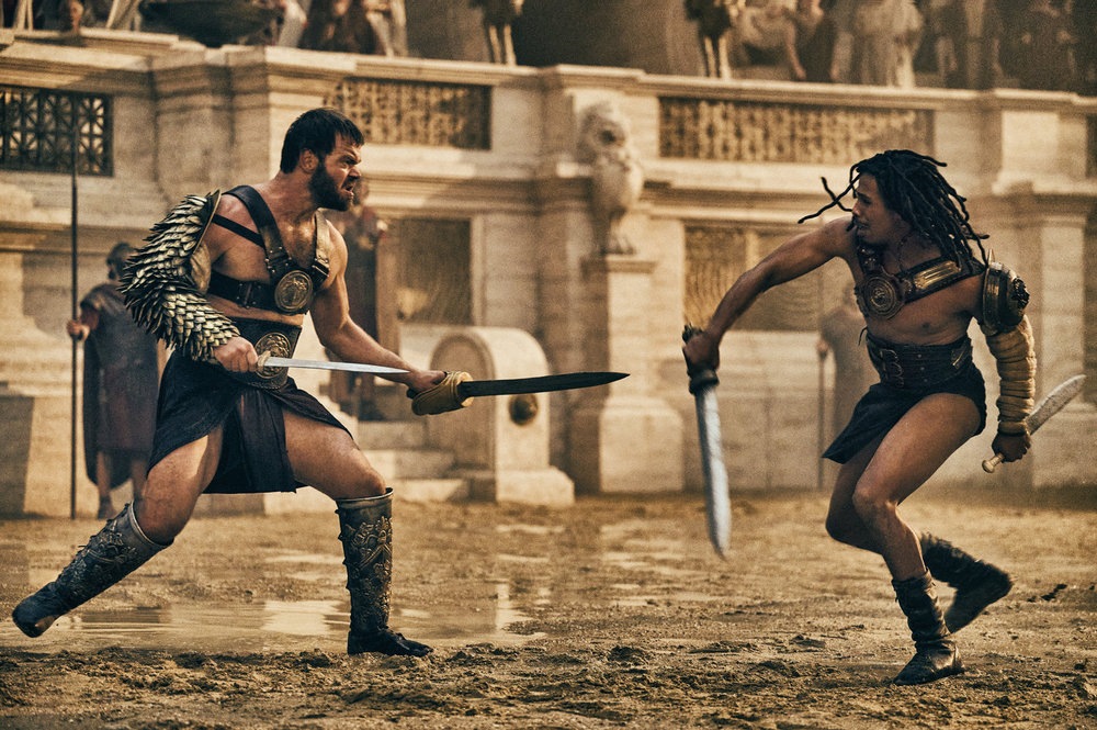 THOSE ABOUT TO DIE, a Peacock series, stars Jóhannes Haukur Jóhannesson as Viggo, Moe Hashim as Kwame, shown here fighting in the gladiator arena