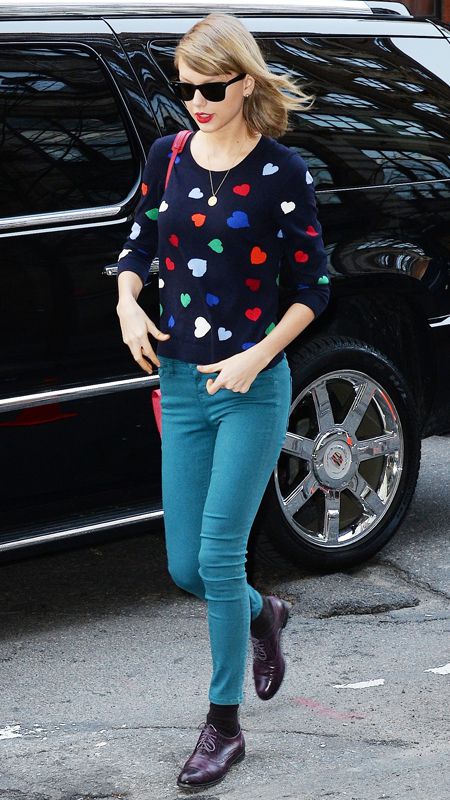 Taylor Swift wearing a multicolored knit with hearts, teal jeans, and aubergine brogues