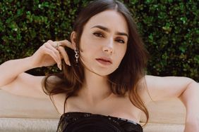 Lily Collins leaning against a wall in a strapless black patterned dress with her hand behind her ear.