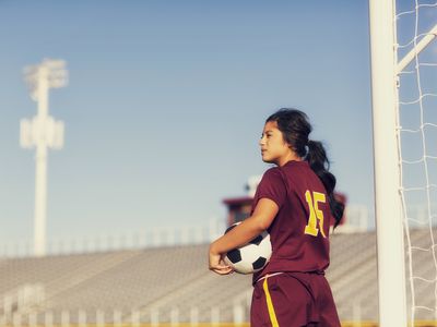 Female high school soccer player holding ball. 