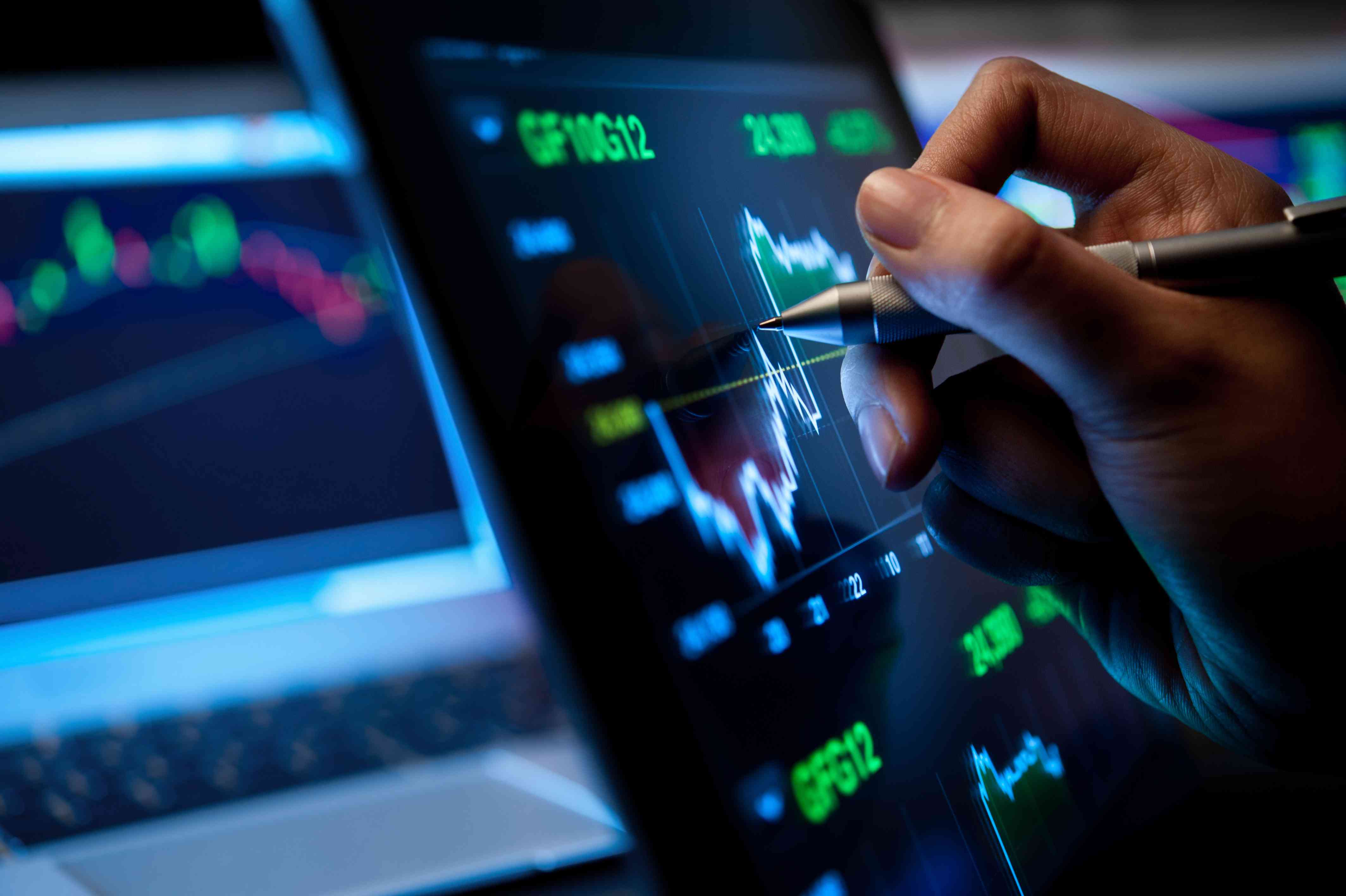 Person using a pen and pointing to a screen with stock data