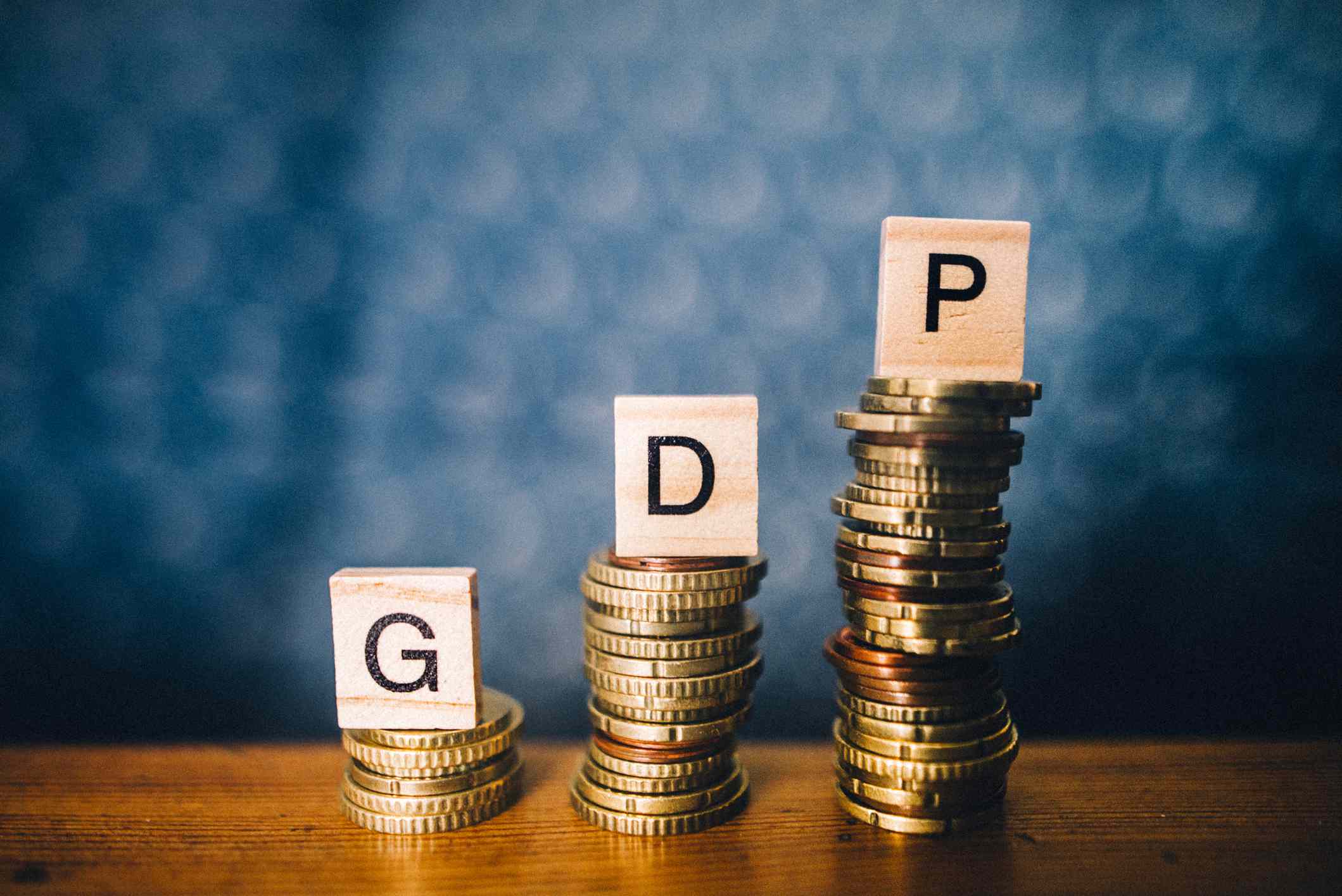 Stacked coins with wooden blocks containing letters on top of them thats spell out "GDP."