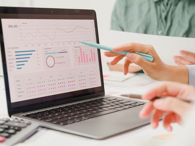 Closeup image of people sitting at a table, with one person pointing to charts on a laptop screen