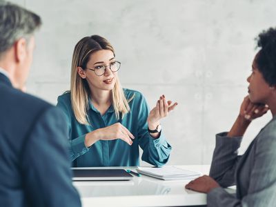 Three people have a discussion in an office setting.