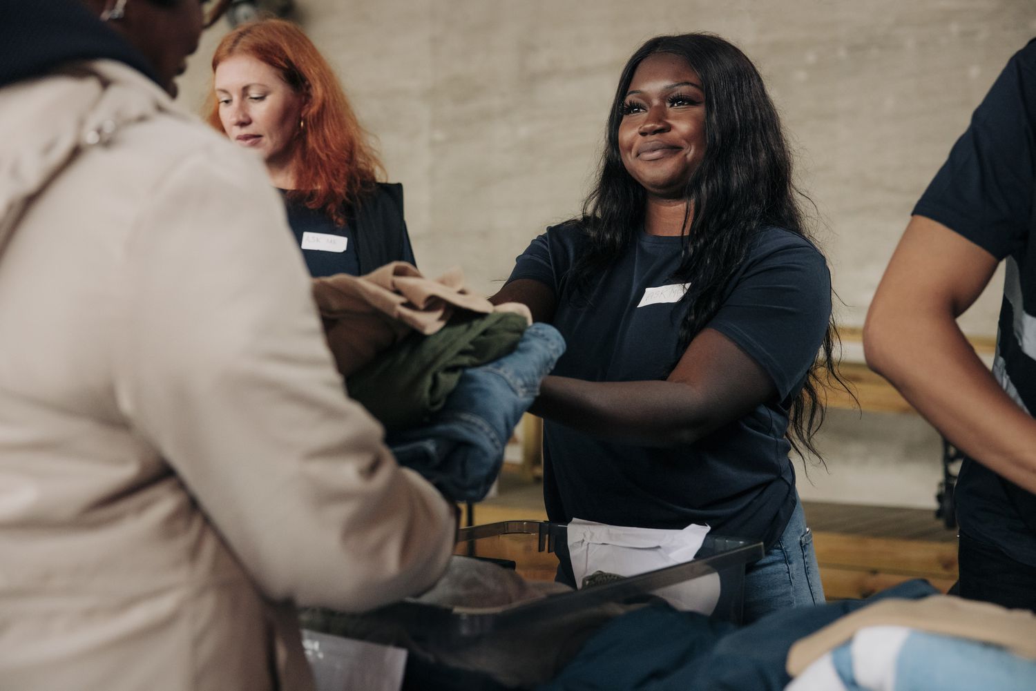 A person handing clothes to a person across a table at a charity.