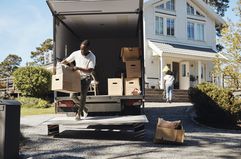 A man unloads boxes from a moving truck outside of a house