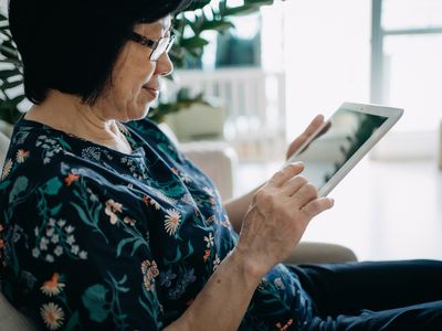 A woman sits on a couch looking at a tablet