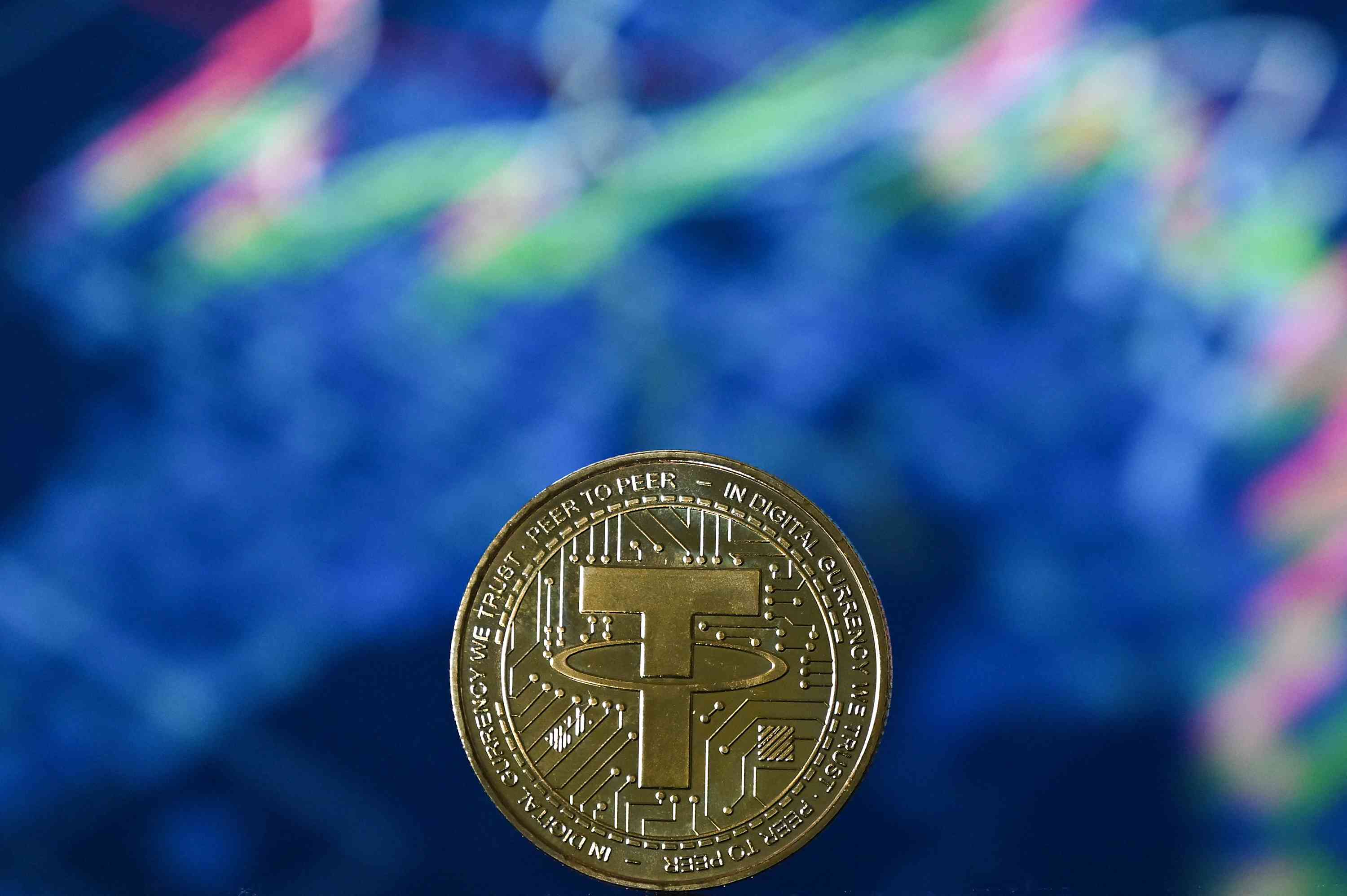 An illustration picture taken in London on May 8, 2022, shows a gold plated souvenir cryptocurrency Tether (USDT) coin arranged beside a screen displaying a trading chart.