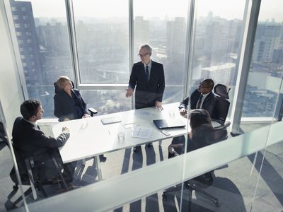 Businessman talking to colleagues in a boardroom meeting with the skyline visible through the windows