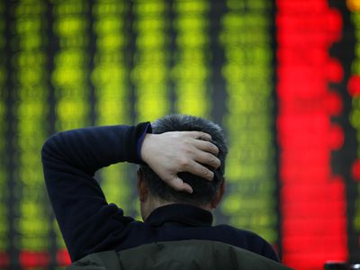 BAck view of an investor holding his head while looking at a ticker board.