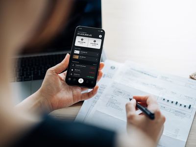 Over the shoulder view of young Asian woman checking online banking on smartphone while handling personal banking and finance at home