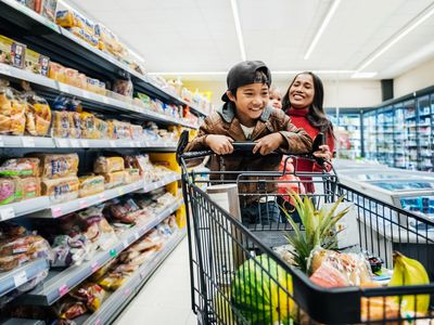 A young boy playing on a shopping cart in a grocery store