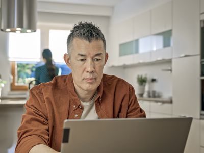 Older man sitting at his kitchen table while looking at a laptop
