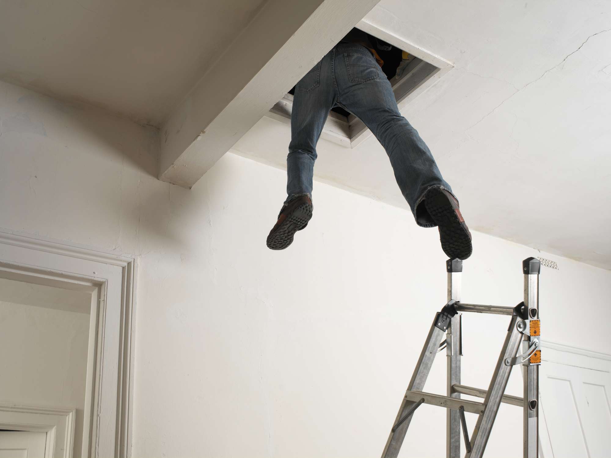 Man dangling out of loft hatch with one foot touching step ladder