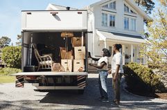 A man and a woman stand next to a moving truck outside of their new house