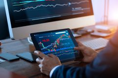 Businessman checking stock market on digital tablet and a desktop computer with stock exchange graph on screen. Financial stock market. Analyzing data in office background.