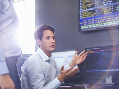 Young businessman in office having a discussion with monitors showing stock data