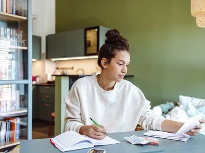 A person sits at a table reviewing bills and taking notes