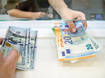 A bank teller and a customer conduct a currency exchange between US dollars and Euro bills.