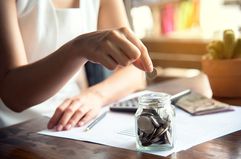 An hand of female putting coin in jar with money stack.