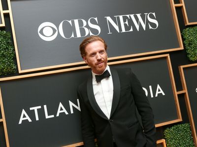 Billions actor Damian Lewis poses in a tuxedo under a CBS News logo