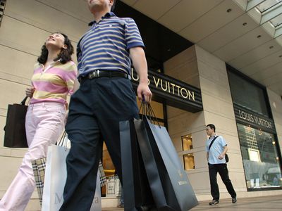 Mainland Chinese tourists loaded with shopping bags walk past a designer brand shop in the Tsim Sha Tsui area of Hong Kong