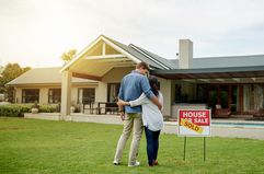 Couple standing next to real estate sold sign at their new house