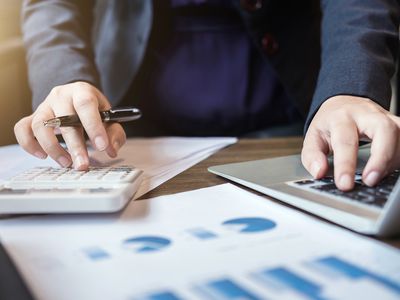 Midsection of Businessman Using Calculator and Laptop at Desk