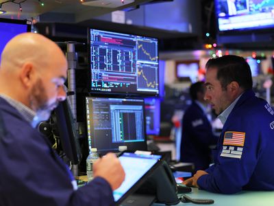 Two traders work on the floor of the New York Stock Exchange in front of stock charts