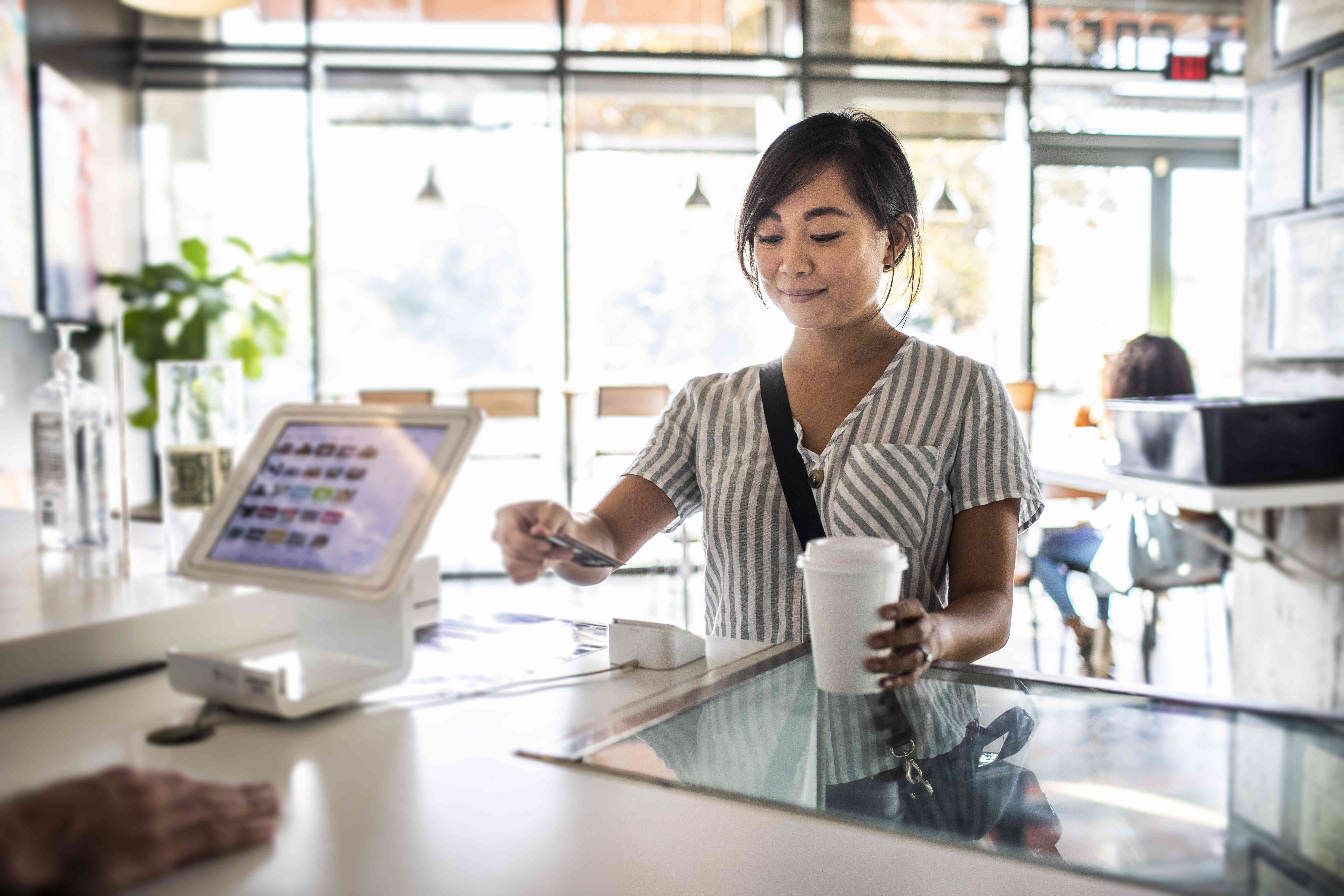 Woman using a credit card reader to pay at a coffee shop counter