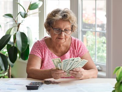 Senior woman sitting at home counting paper money and some pennies