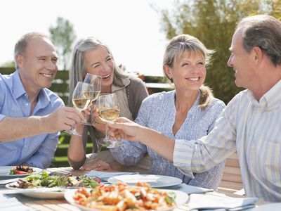 Two senior couples toast with glasses of wine.